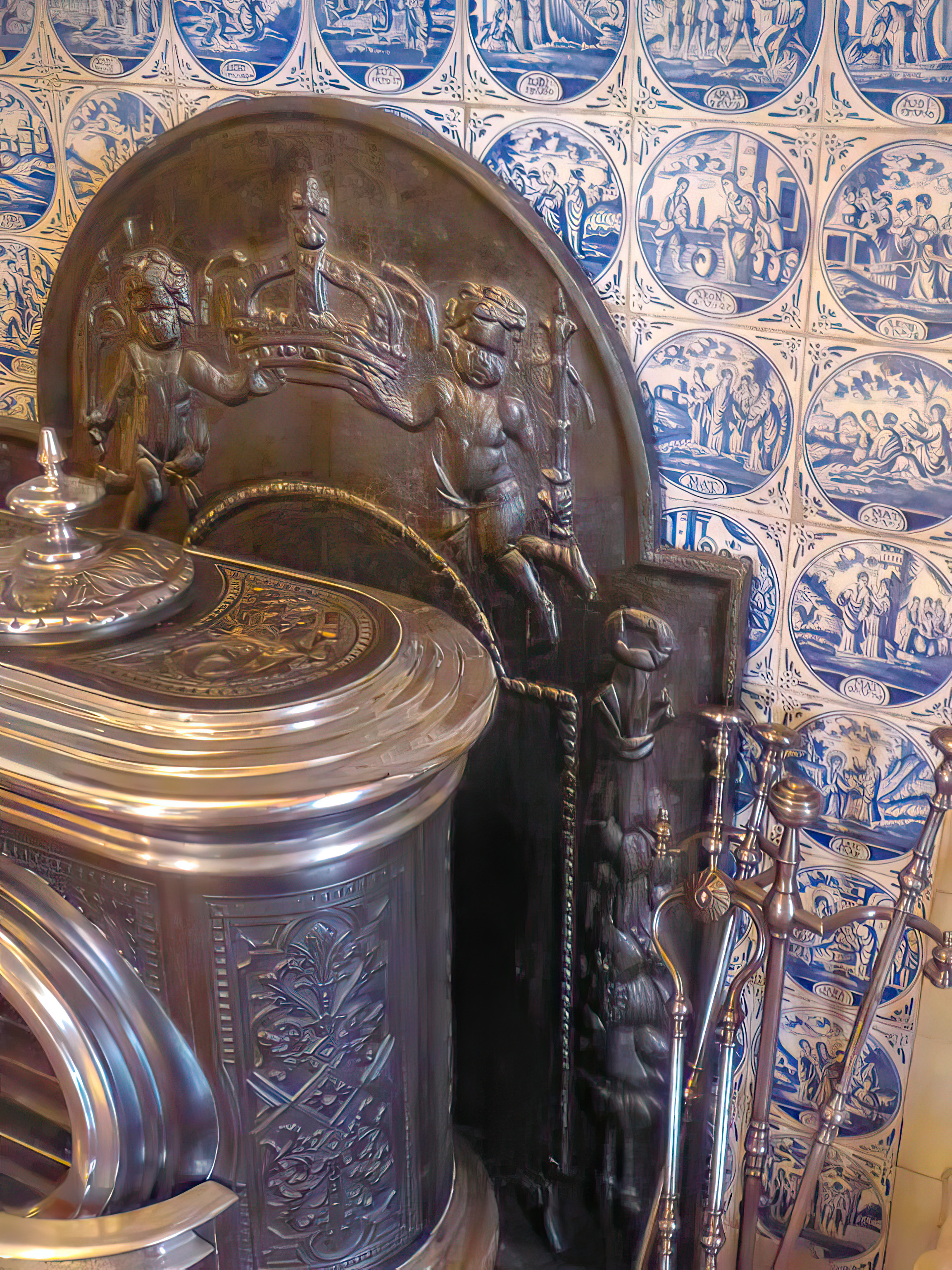 Close up of a fireback behind a stove with a fireplace toolset in front